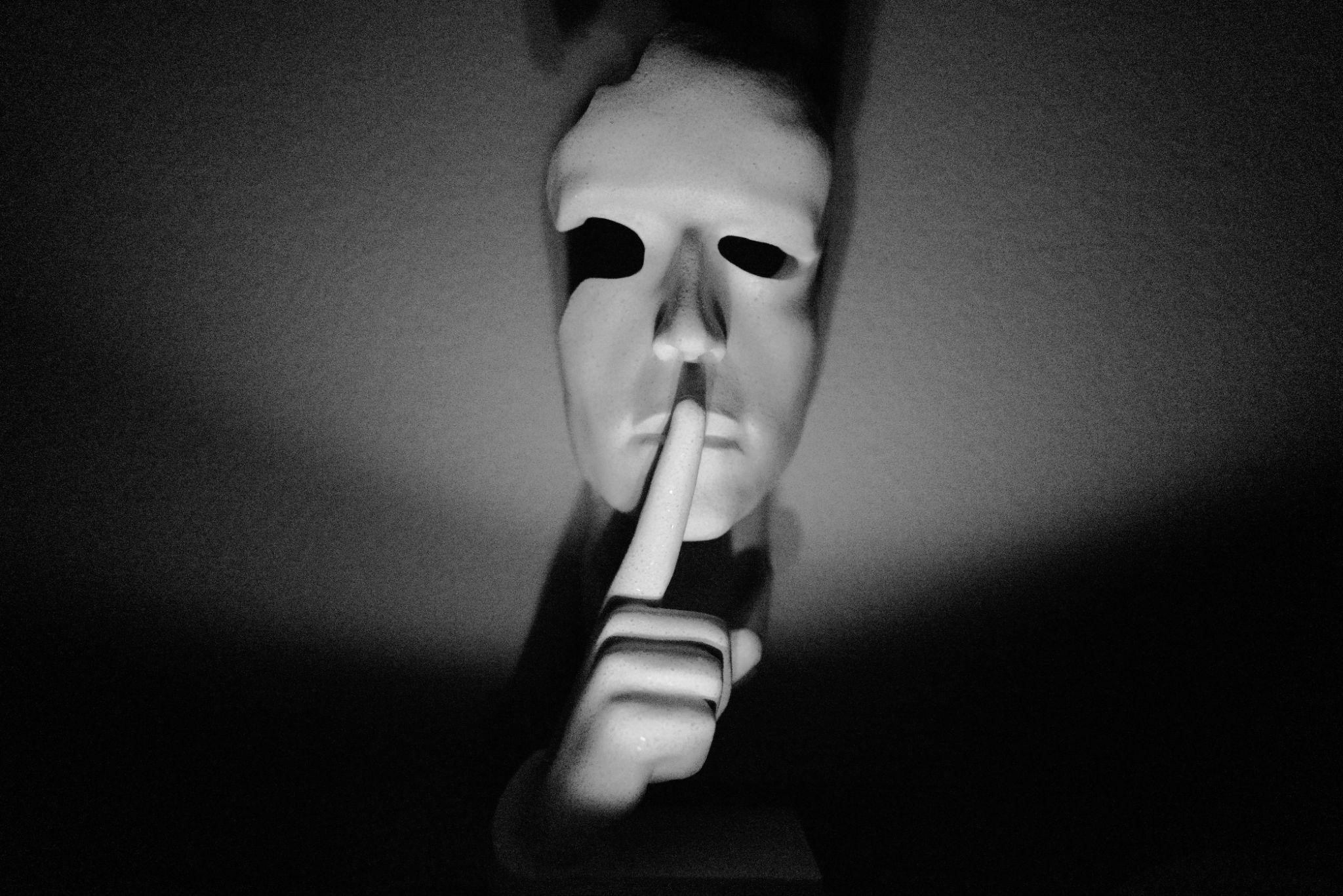 davidstewartGWO A person in a mask with his index finger over his lip, depicting mystery and thriller in the dark world of human trafficking in suspense fiction.