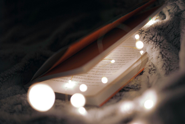 An open book rests on a blanket, surrounded by glowing lights.