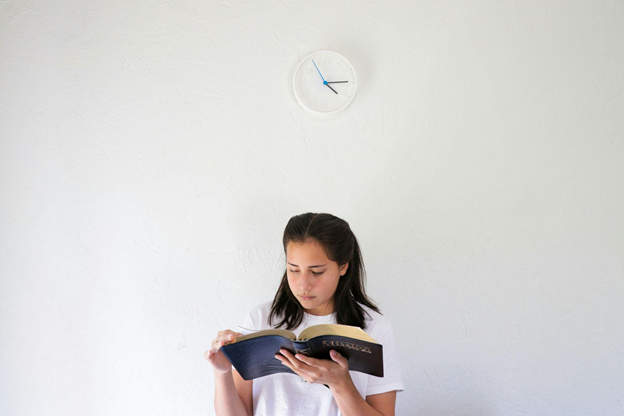 A woman reads a large book against a plain white wall.
