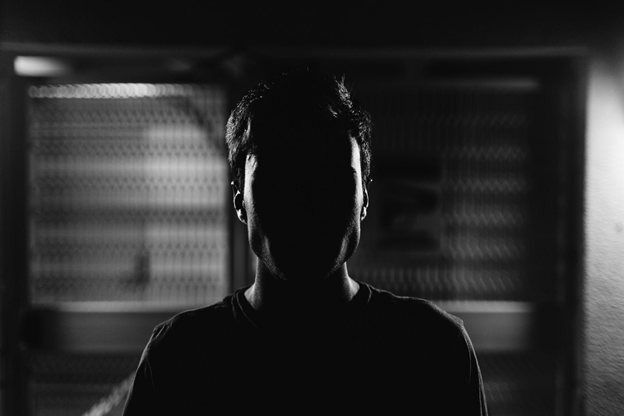 Silhouette of a person against a textured, grid-like background, creating a mysterious atmosphere.