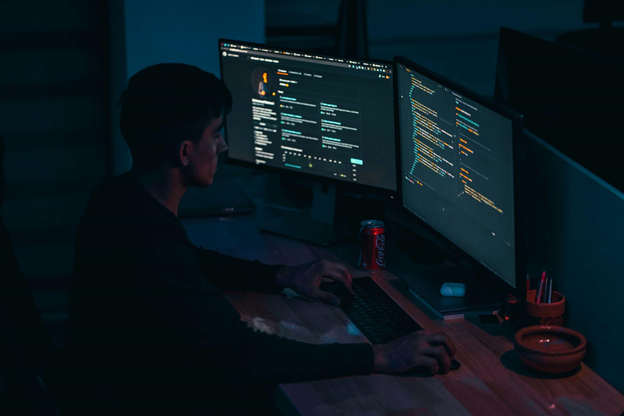 A person works at a desk with two computer monitors displaying code and a dark-themed webpage.